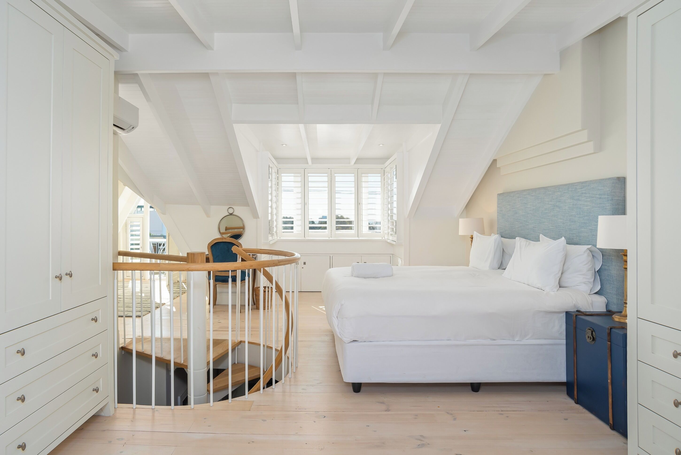 Une chambre à coucher avec un grand lit, un escalier en bois et une vue sur la ville grâce à de grandes fenêtres.