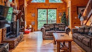 A log cabin interior with a high ceiling, a fireplace, a sofa, a coffee table, and a Christmas tree.