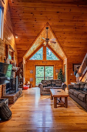 A log cabin interior with a high ceiling, a fireplace, a sofa, a coffee table, and a Christmas tree.