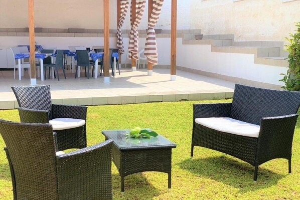 An outdoor patio area with wicker furniture and a table, a covered seating area with tables and chairs, and a staircase leading to an upper level.