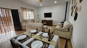 Un comedor con una mesa preparada para cuatro personas, un sofá, un televisor y una pared decorada con platos.