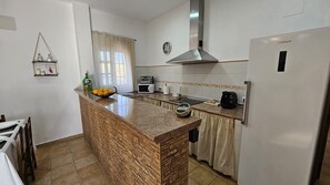 Una cocina con isla de granito, campana extractora de acero inoxidable, refrigerador y ventana con cortinas.