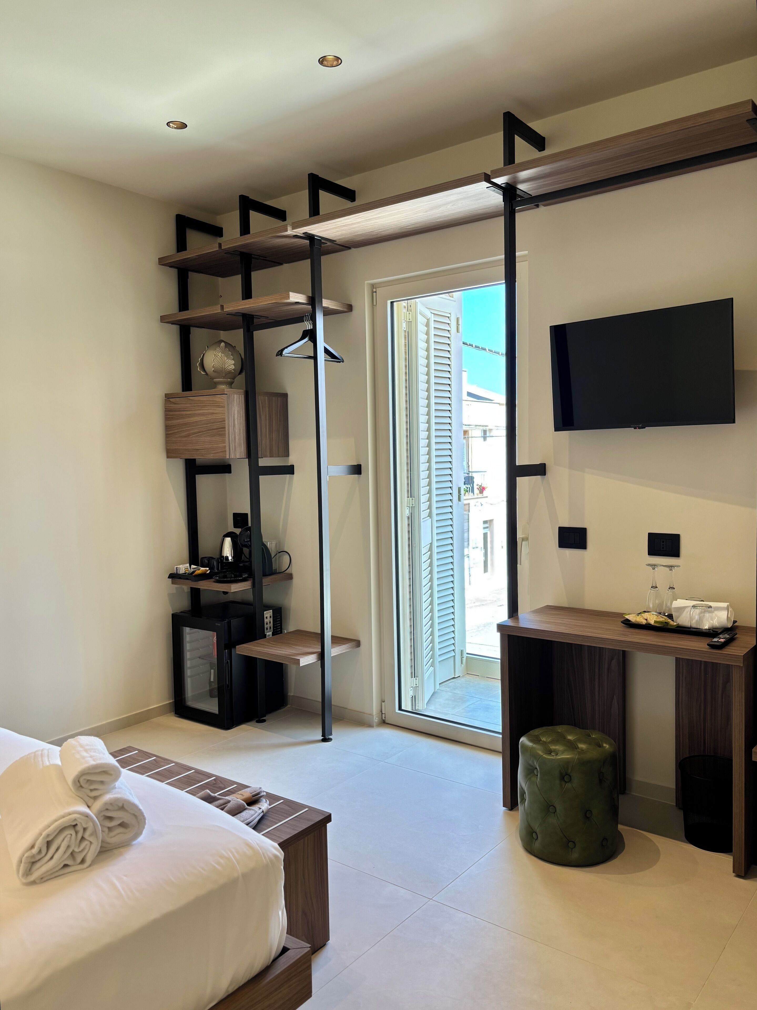 Une chambre d’hôtel moderne équipée d’un lit, d’un bureau, d’une télévision et d’une porte coulissante donnant sur l’extérieur.