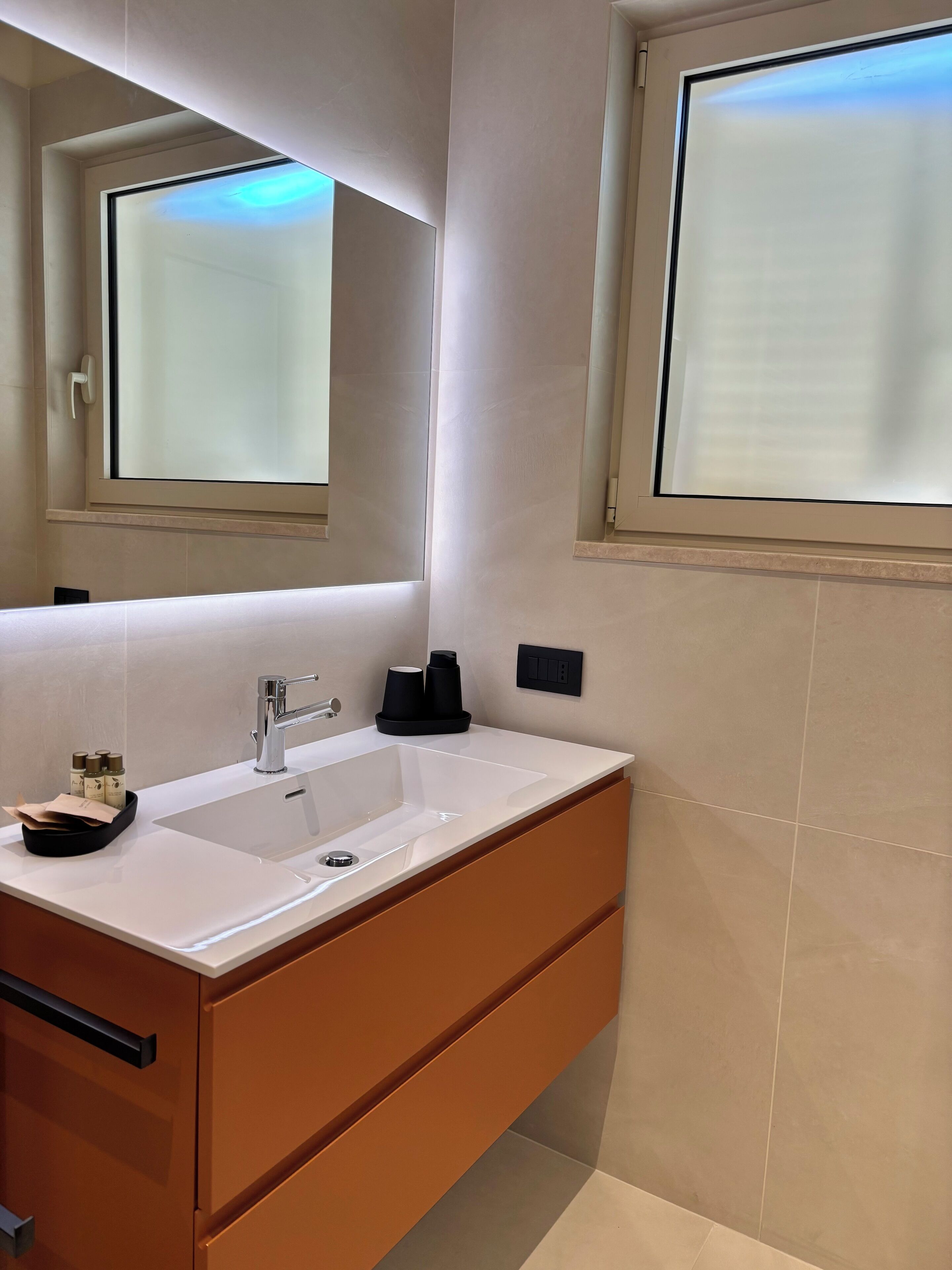Un baño moderno con un lavamanos blanco, un espejo y una ventana.