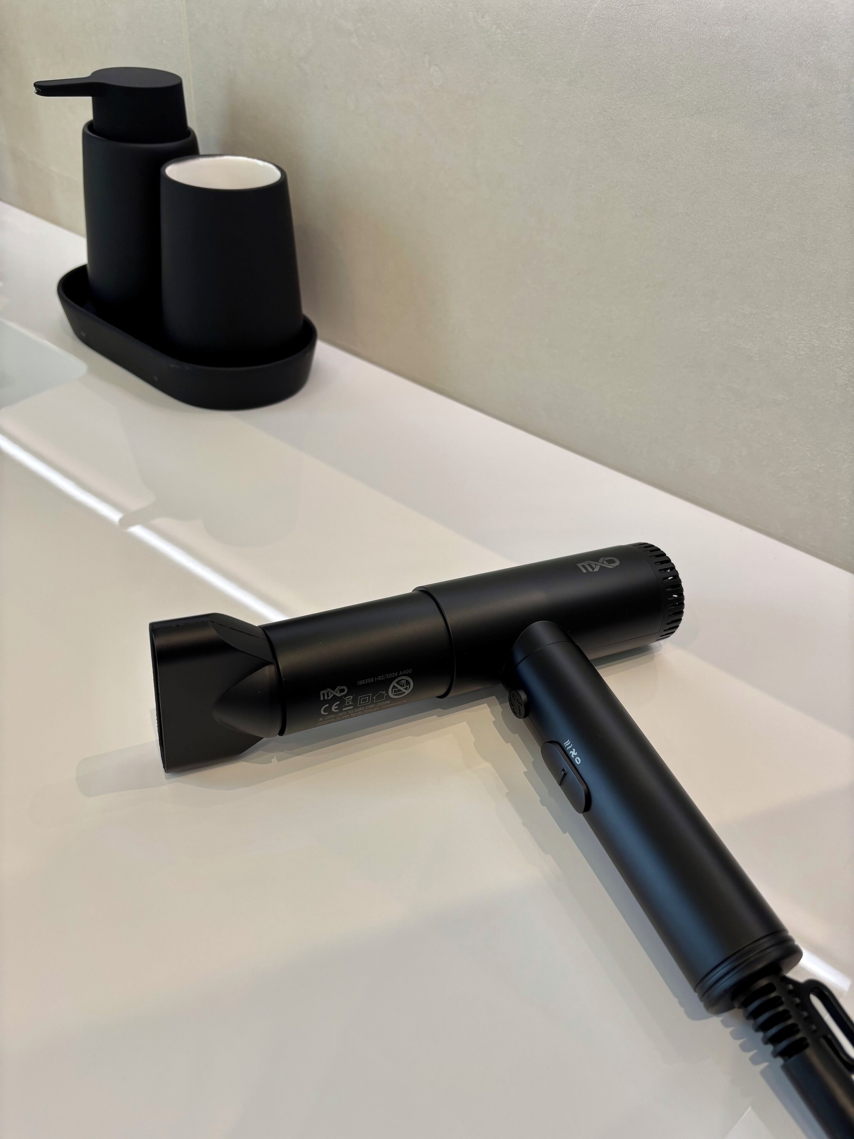 Un aspirateur noir est posé sur une surface blanche. À l’arrière, on aperçoit une pompe noire et un récipient blanc.