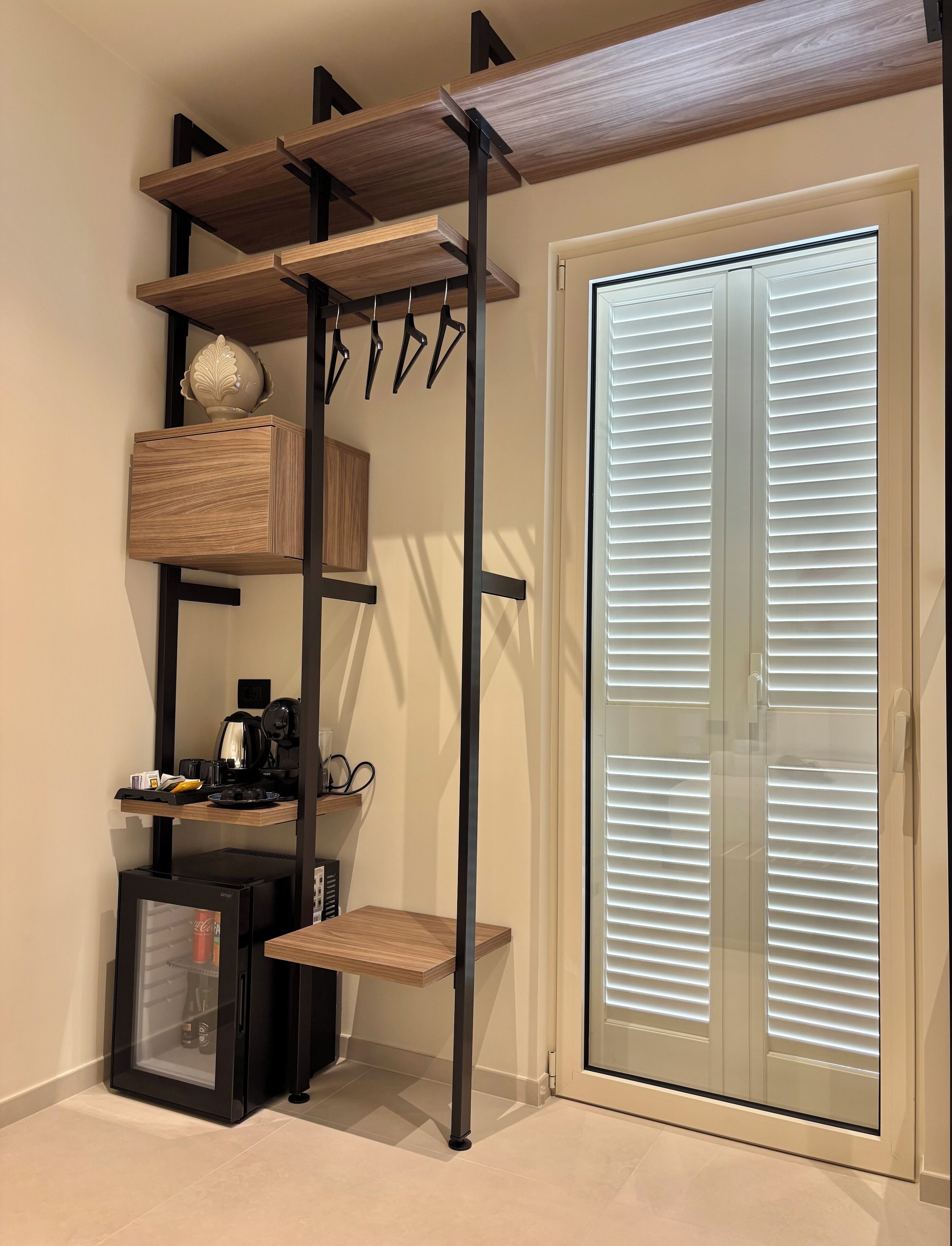 A compact room with a built-in shelving unit, a small coffee station, and a sliding glass door closet.