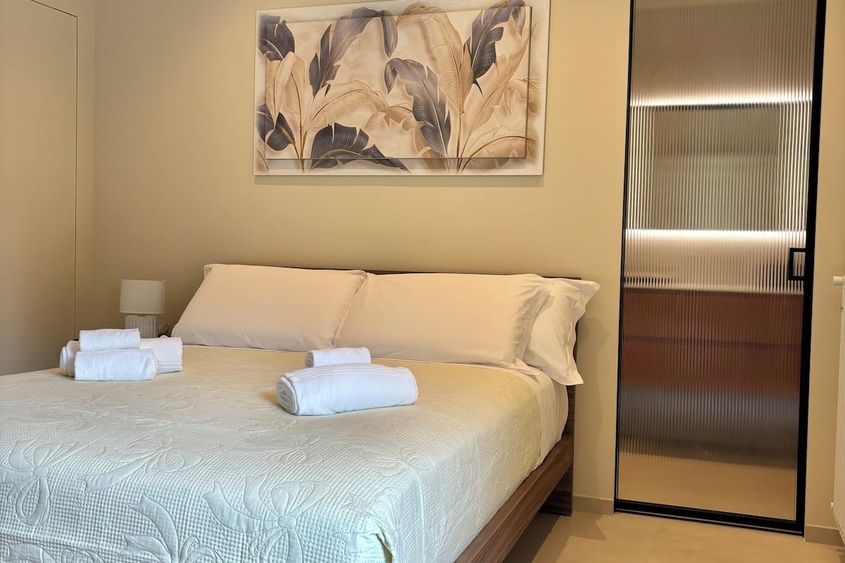 Un dormitorio moderno con una cama grande, una mesita de noche, una obra de arte en la pared y una puerta corredera.