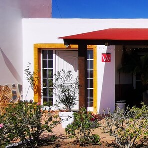 A building with a white facade, yellow trim, and a red awning. There is a door with glass panels and a sign with a 'V' logo.