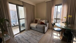 A modern living room with a sofa, a glass dining table, and a view of the city through large windows. - TrevizZo Aero Congonhas (São Paulo)