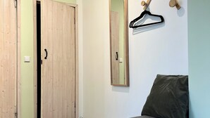Ein Zimmer mit Holzboden, einer grauen gepolsterten Bank, einem hölzernen Haken an der Wand und einer Tür mit Griff.