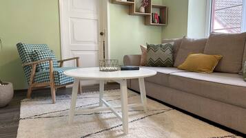 A living room with a beige sofa, a patterned armchair, a white coffee table, and a bookshelf against the wall.