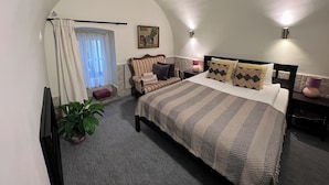 Ein Schlafzimmer mit einem großen Bett, einem Sessel, einem kleinen Tisch, einer Pflanze und einem Bild an der Wand.