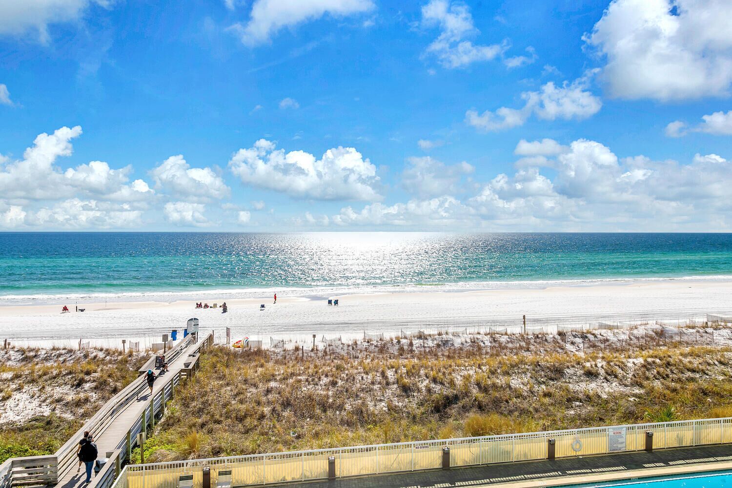 A beach with a wooden boardwalk leading to the shore, a clear sky, and the ocean.