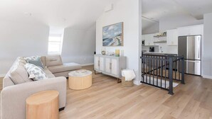 Ein modernes Wohnzimmer mit einer Couch, einem runden Couchtisch und einem Essbereich mit Küche im Hintergrund.