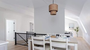 A dining area with a white table and chairs, a hanging wicker light fixture, and a staircase with a black railing. - Downtown Newport Penthouse (Newport)