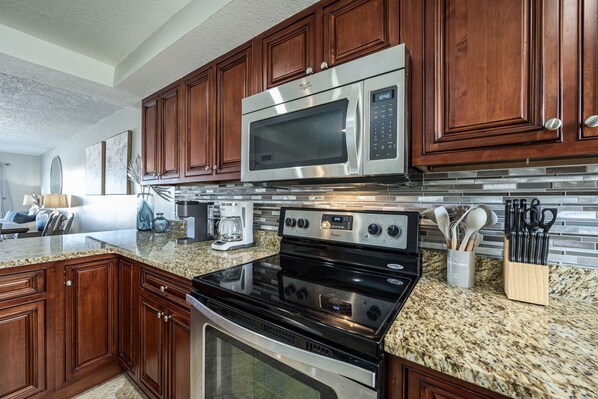 A modern kitchen with wooden cabinets, stainless steel appliances, granite countertops, and a built-in oven.