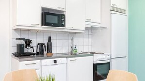 A modern kitchen with white cabinets, a microwave, a coffee maker, a sink, a dishwasher, and an oven. - Oma Hotelli  (Ylojarvi)