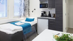 A compact room with a bed, a small kitchenette, a white table, and a potted plant. - Oma Hotelli  (Ylojarvi)