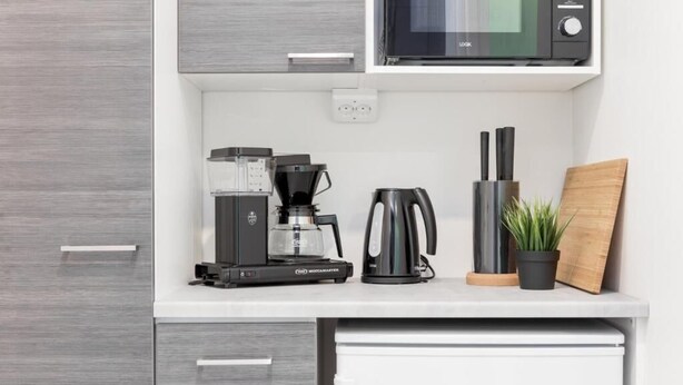A kitchenette with a coffee maker, a kettle, a microwave, and a cutting board. - Oma Hotelli  (Ylojarvi)