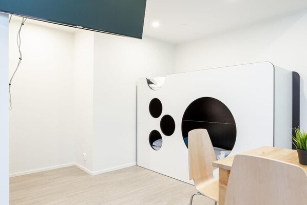Un espacio de oficina moderno con un divisor blanco que tiene recortes circulares, una mesa de madera y dos sillas.