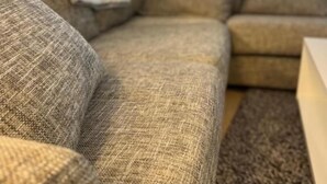A sectional sofa with a textured fabric, a throw blanket, and a woven rug. - Oma Hotelli  (Ylojarvi)