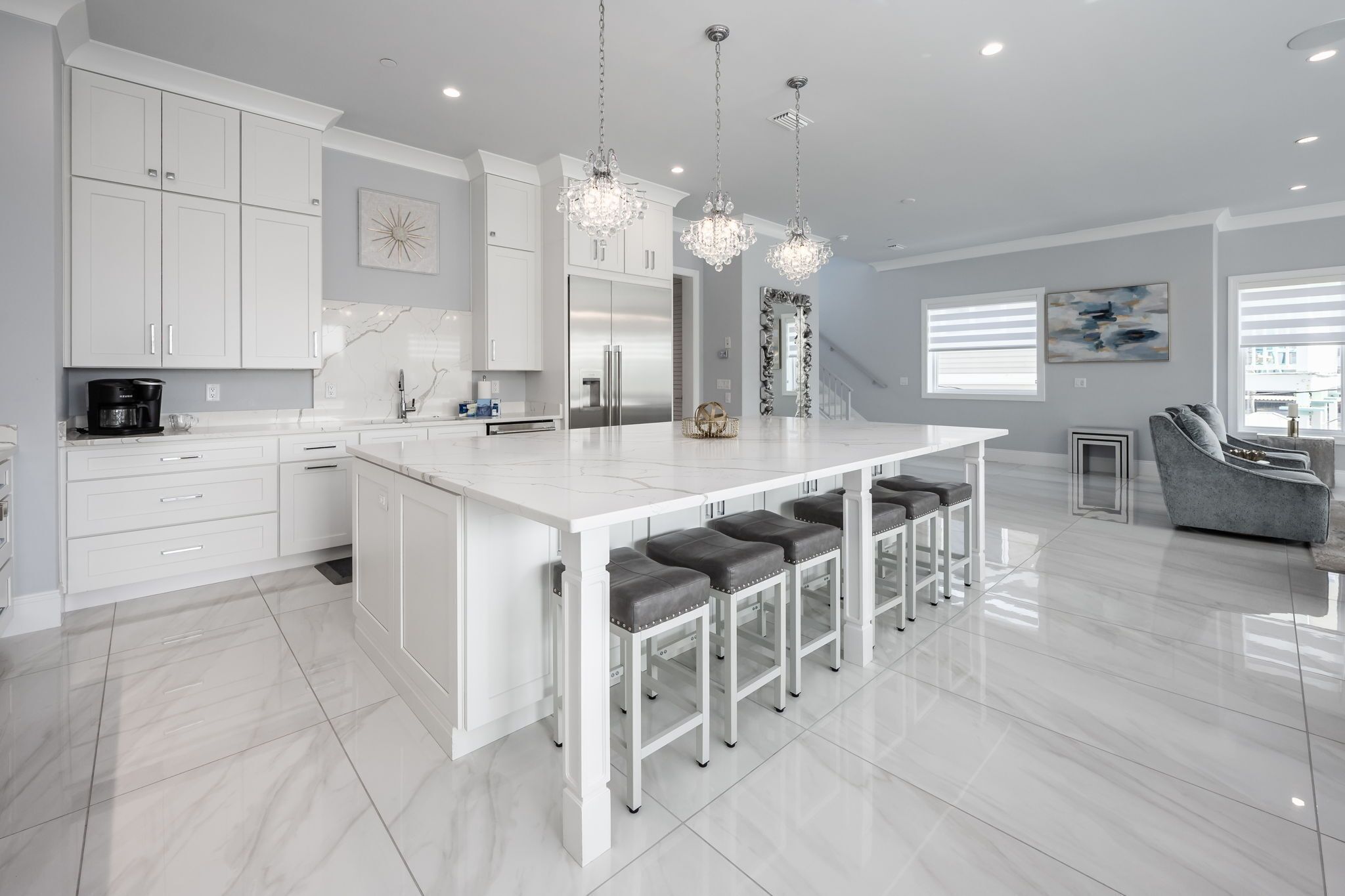 A modern kitchen with white cabinetry, a central island with bar stools, stainless steel appliances, and pendant lighting.