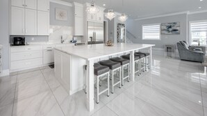 Une cuisine moderne avec des meubles blancs, un îlot central doté de tabourets de bar, des appareils en acier inoxydable et un éclairage suspendu.