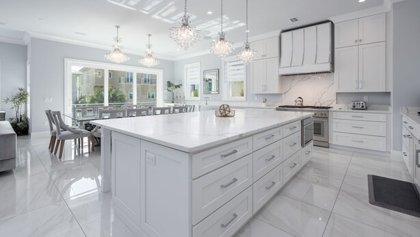 Une cuisine moderne avec des meubles blancs, un grand îlot central et des luminaires suspendus.