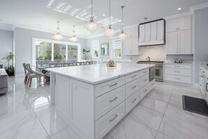 Une cuisine moderne avec des meubles blancs, un grand îlot central et des luminaires suspendus.