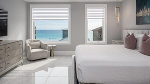 Une chambre moderne avec un grand lit, une vue sur la mer, un téléviseur et un tableau représentant un paysage urbain.