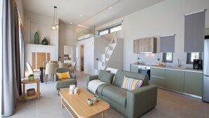 A spacious living area with a sofa, coffee table, and dining table. A kitchen with a countertop and cabinets is visible in the background. - Efxenia Villas-Villa Luna (Lefkada)