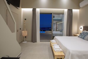 A hotel room with a bed, a bench with towels, a suitcase, and a view of a pool at night. - Efxenia Villas-Villa Luna (Lefkada)