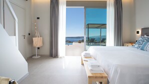 A modern hotel room with a large bed, a bench with towels, a view of the outdoors, and a balcony with a pool. - Efxenia Villas-Villa Luna (Lefkada)