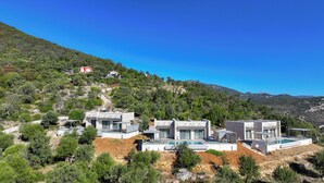 En ejendom på en skråning med moderne huse, en swimmingpool og en rød bygning i baggrunden.