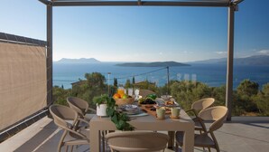 En terrasse med et bord dækket til morgenmad, med udsigt over et smukt hav- og landskab.