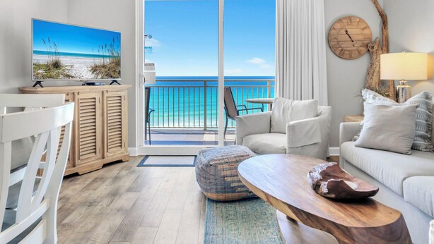 A room with a view of the ocean, a television, a wooden coffee table, and a sofa.
