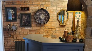 Een kamer met een bakstenen muur, een blauwe kast, een klok, een lijst met een afbeelding, een spiegel en een lamp.