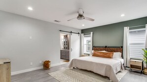 Een slaapkamer met een bed, een plafondventilator, een raam met gordijnen en een klein nachtkastje.