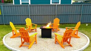 Een rond zitgedeelte buiten met zes Adirondack-stoelen rond een vuurkuil.