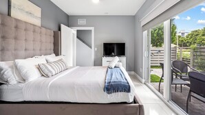 Ein Schlafzimmer mit einem großen Bett, einem Fernseher und einer Glastür zum Balkon.