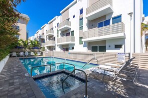 Une piscine dotée d’une terrasse carrelée, entourée d’immeubles modernes à plusieurs étages et dotés de balcons.
