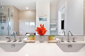 Une salle de bain moderne avec deux vasques, un grand miroir et un vase rempli de fleurs rouges.