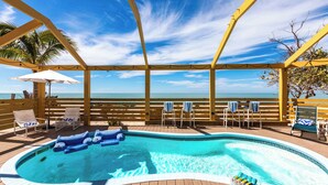 Um deck de madeira com hidromassagem, cadeiras de descanso e guarda-sóis, com vista para a praia.