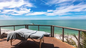 Um deck de madeira com uma mesa de massagem, com vista para uma praia e oceano.