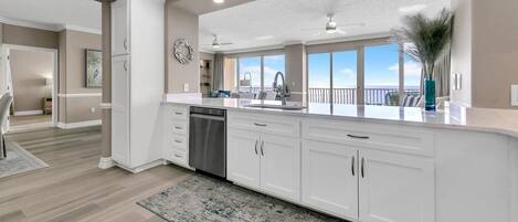 A modern kitchen with white cabinetry, a dishwasher, and a large window offering a view of the outdoors.