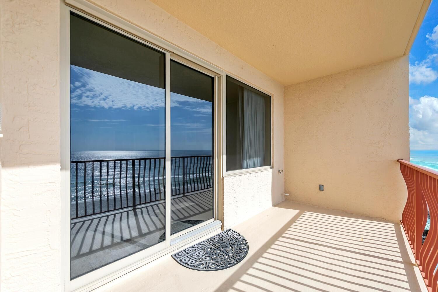 Un balcon avec vue sur l’océan, une porte-fenêtre coulissante et une rambarde rouge.