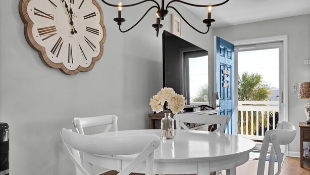 A dining area with a round white table, white chairs, a large wall clock, and a chandelier. - Perfect Surf City Stay: Walk to Beach, Dining, & Fun (Surf City)