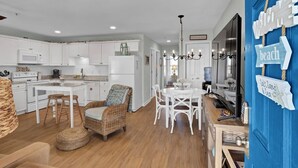 A modern kitchen with white cabinets, a dining area with white chairs, and a wicker chair. - Perfect Surf City Stay: Walk to Beach, Dining, & Fun (Surf City)