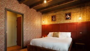 Une chambre d’hôtel avec un grand lit, une tête de lit en bois, des murs décorés d’un motif en briques et deux tableaux encadrés accrochés au mur.