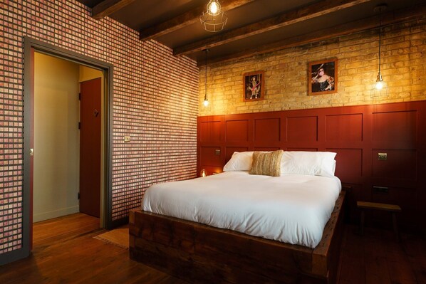 A hotel room with a large bed, wooden headboard, brick-patterned walls, and two framed pictures on the wall. - GuestReady - Charming Studio in Central London (London)